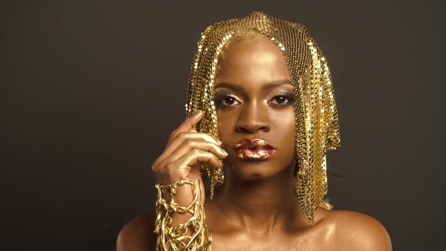 Surreal Portrait of Glossy African American Woman with Bright Golden Makeup. Bronze Bodypaint