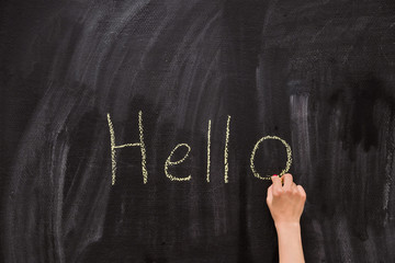 Closeup of child's hand writing Hello word with chalk on the backboard in school class. Education, elementary school, learning, back to school concept. schoolboy writing on chalk board in classroom.