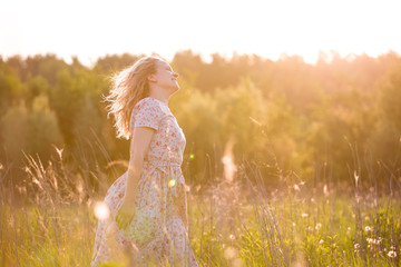 Portrait of happy young blond woman running on a meadow on a sunny summer day. Girl dancing on the...