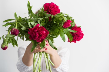 Woman holding beautiful red peonies. Girl with bouquet of flowers in her hands. Closeup of hands holding peonies.