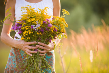 Closeup of woman's hands holding beautiful bunch of wild flowers on a sunny summer day. Girl with...