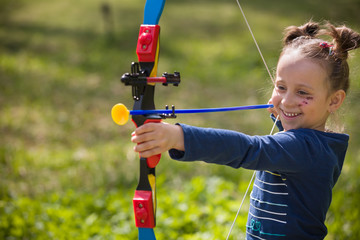 Cute girl archer with bow shooting in sunny summer day. little girl shoots bow in the park....