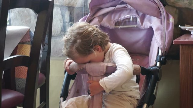 Cute little child seating in the baby carriage, very tired and wants sleep.