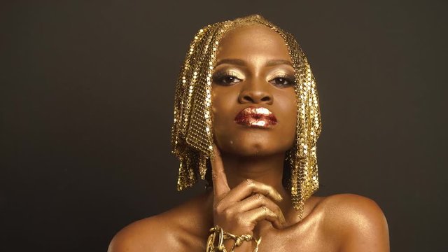 Studio Portrait of Surreal African American Woman with Golden Faceart Preapring For Shooting With Stylist. Creative Vogue Concept