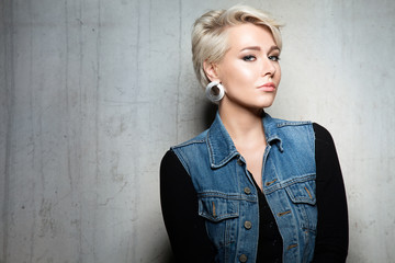 Portrait of a woman with short hair in jeans jacket with large earrings on a gray cement background