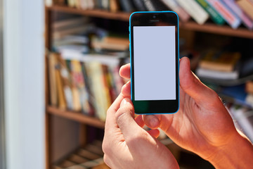 Hands holding mobile phone on the background of bookshelves