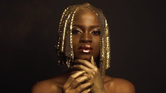 Reflexion. Portrait of glossy african american female model with bright glossy golden makeup posing on black studio background. High fashion shooting, Vogue concept