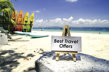 conceptual image,white canvas frame and wooden easel with word BEST TRAVEL OFFERS. Tropical beach  at sunny day ,white sand,colorful kayaks and clear blue water background. - 112424925