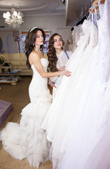 Naklejka premium Female trying on wedding dress in a shop with women assistant.