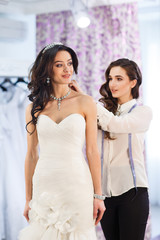 Naklejka premium Female trying on wedding dress in a shop with women assistant.