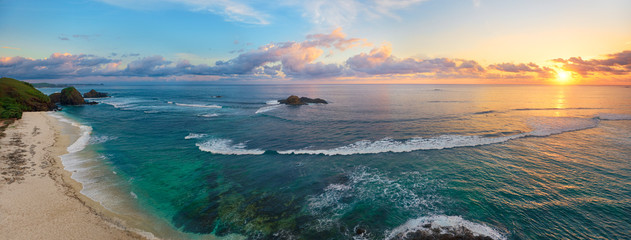 Panoramisch uitzicht op tropisch strand met surfers bij zonsondergang.