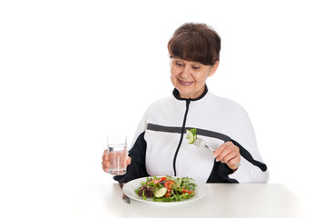 Elderly woman in sport costume eating green salad. Healthy life style concept