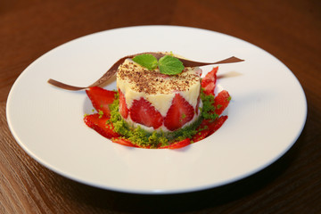 layered dessert with strawberries, biscuit cake and cream cheese on a dark wood background
