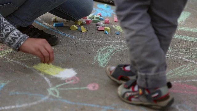 Children draw pictures with colored chalk on the asphalt
