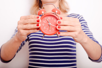 Female in striped shirt holding red alarm clock