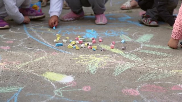 Children draw pictures with colored chalk on the asphalt
