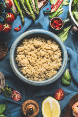 Cooked quinoa  in blue bowl with delicious seasonal vegetables and ingredients for salad making on dark background, top view, close up. Superfood , healthy eating or vegetarian food concept.