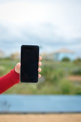 Female holding smart phone in hand on outdoors background. Blank screen with copyspace