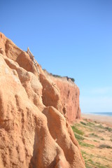 Fototapeta na wymiar Red rock wall with defocused beach and ocean. Sunny outdoors background
