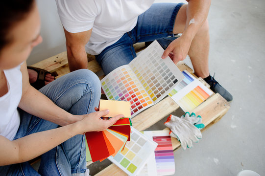 Two persons choose color of decor, sitting on the wooden pallet at a cement floor.