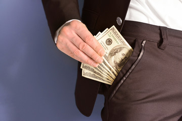 Man getting dollar banknotes out of suit pocket on grey background