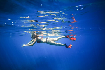 The girl floats on the surface of the ocean with snorkel and fins. Photo underwater