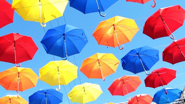 Multicolored umbrellas hanging over head on the street against the blue sky and swinging in the wind
