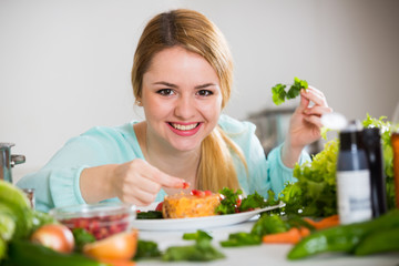 Young woman decorating salad with herbs in kitchen