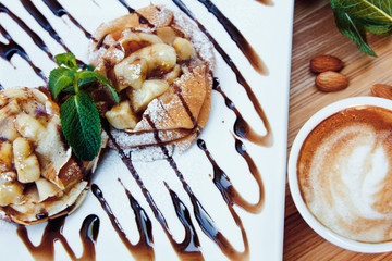 pancakes with chocolate and fruit and coffee on wooden background. Beautiful restaurant serving the dessert