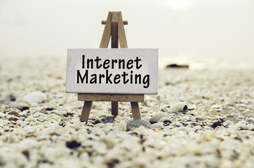 conceptual image with word INTERNET MARKETING on white canvas frame with wooden tripod stand.Blurred Clamshell and cockles background.