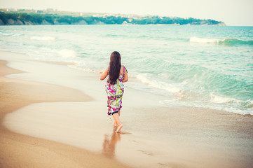 Rear view of child walking along the seacoast. Girl in a colorful dress walking on the beach