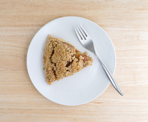 Top view of a slice of Dutch apple pie on a plate with a fork atop a wood table top.