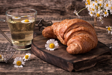 Breakfast with herbal tea and croissant on wooden vintage table