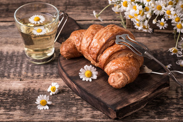 Breakfast with herbal tea and croissant on wooden vintage table