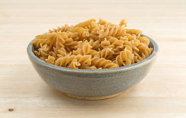 Fusilli whole wheat organic pasta in an old bowl atop a wood table.