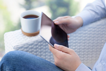 man sitting in summer cafe and holding tablet computer