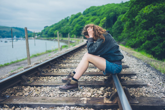 Sad young woman sitting on railroad tracks