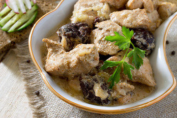 Meat stew with prunes and potato garnish on a wooden table.