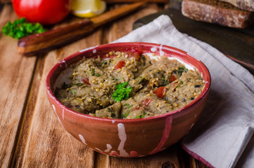 Babaganoush with tomatoes, cucumber and parsley - arabian eggplant dish or salad on wooden background. Selective focus