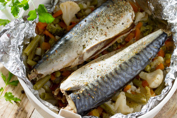 Tasty baked fish with vegetables in foil on a wooden table, a he