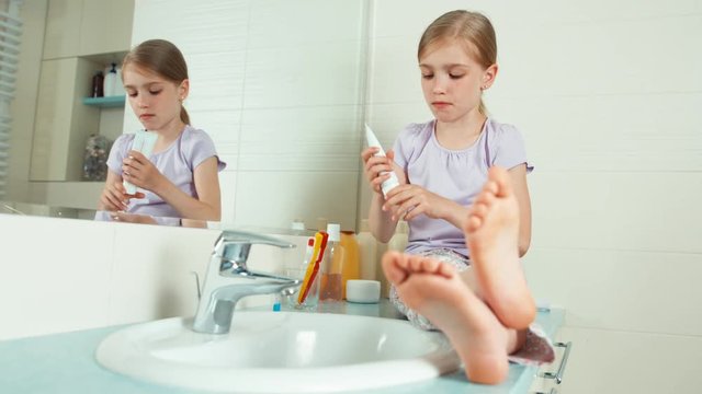 Girl using toothbrush and toothpaste while sitting near a mirror