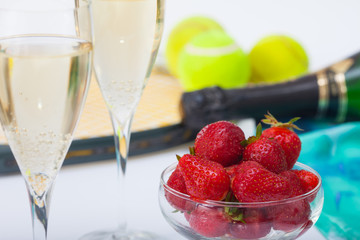  Strawberries, champagne and tennis balls in front of racket on the table