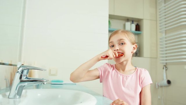 Portrait girl child 7-8 years old cleaning teeth in bathroom and looking at camera
