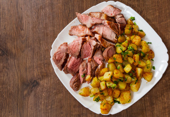 Sliced medium rare grilled Steak Ribeye with potato in a plate on wooden table