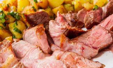 Sliced medium rare grilled Steak Ribeye with potato in a plate on wooden table