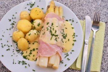 Boiled white asparagus with the ham and fresh new boiled potatoes served with the hollandaise sauce and small pieces of choped chives. Very healthy fresh seasonal dish typical for german cuisine.
