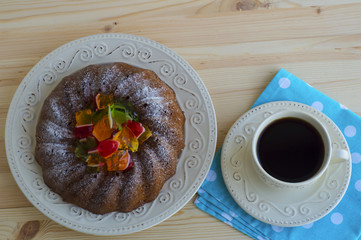 Ring cake with pieces of jelly and cup of coffee on blue cotton, flat lay.