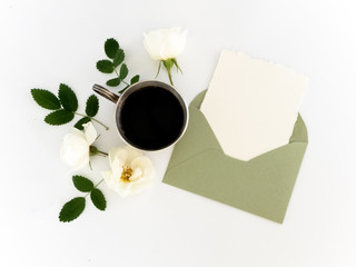 Cup of coffee, blank paper in the envelope, pen and flowers. flat lay, top view