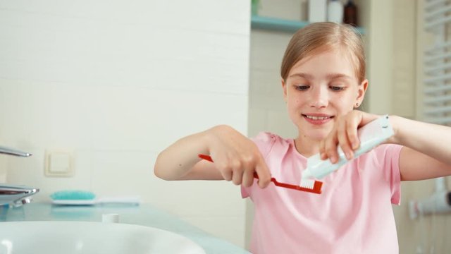 Close up portrait girl 7-8 years old cleaning teeth with toothpaste and smiling at camera. Child puts toothpaste on the brush