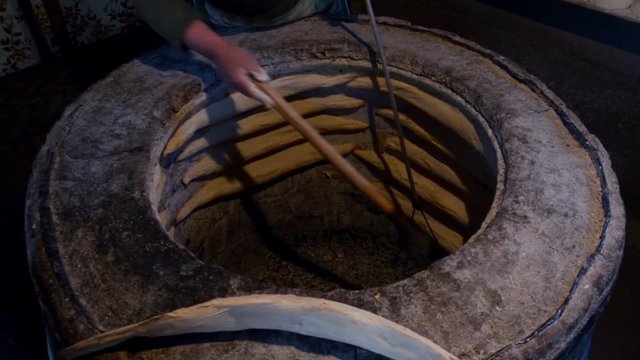 In a large tandoor woman prepares a traditional Georgian bread shoti
